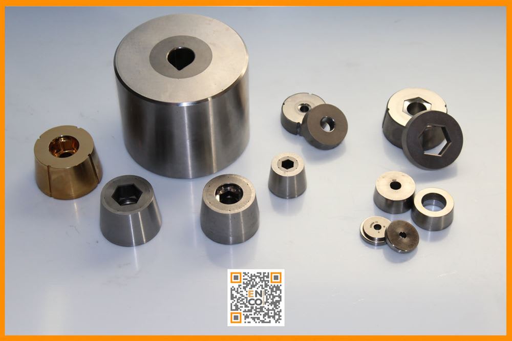Assortimento di matrici e inserti in metallo, lucidi e bronzo, di varie forme e dimensioni, con fori rotondi, esagonali e sagomati per lavorazioni industriali.