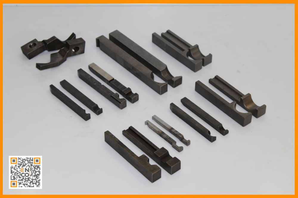 Assortimento di componenti metallici industriali lavorati con precisione, tra cui barre, inserti e utensili con varie scanalature, profili e attacchi.