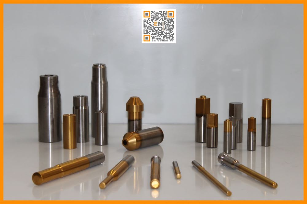 Assortimento di componenti meccanici di precisione in acciaio lucido e ottone dorato, con diverse finiture bicolore, disposti su una superficie chiara e riflettente. Nell'angolo superiore è presente un QR code con il logo ENCO.