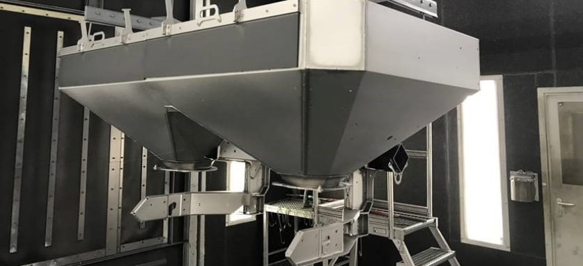 Industrielle Schüttgut-Dosieranlage mit zwei großen grauen Trichtern und integrierten Wiegeeinheiten in einer Produktionshalle.