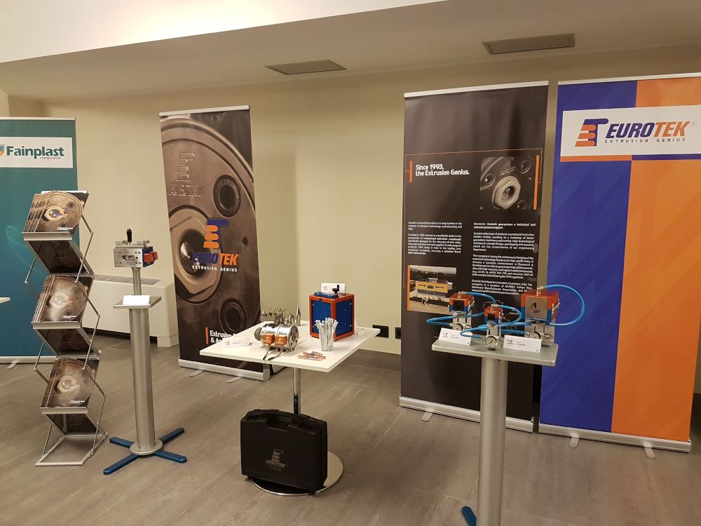 Stand espositivo delle aziende Eurotek e Fainplast con banner promozionali, display di componenti per estrusione e modelli di macchinari industriali.