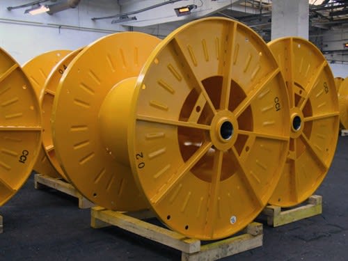 Grandi bobine industriali gialle vuote per cavi, allineate su supporti in legno in un magazzino.