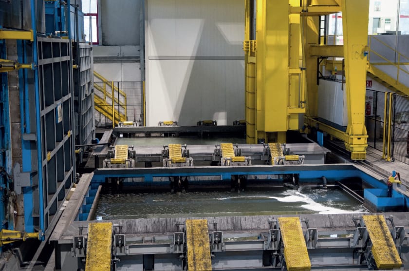 Automated industrial facility with large tanks for metal surface treatment, featuring yellow gantry cranes moving parts through multiple liquid processing baths.