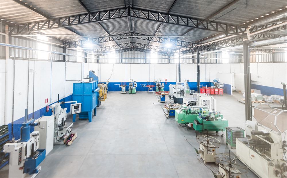 Clean and well-lit industrial factory interior with rows of various manufacturing machinery, blue and white walls, and a metal truss ceiling.