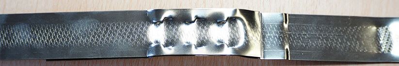 Flexible metal strap with diagonal textured patterns on both ends and corrugated, spring-like bends in the center