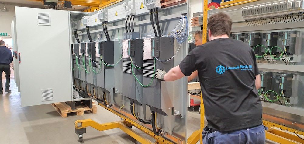 Factory workers from Lanneå Bruk AB assembling multiple industrial electrical control panels, featuring Siemens drives and intricate wiring.