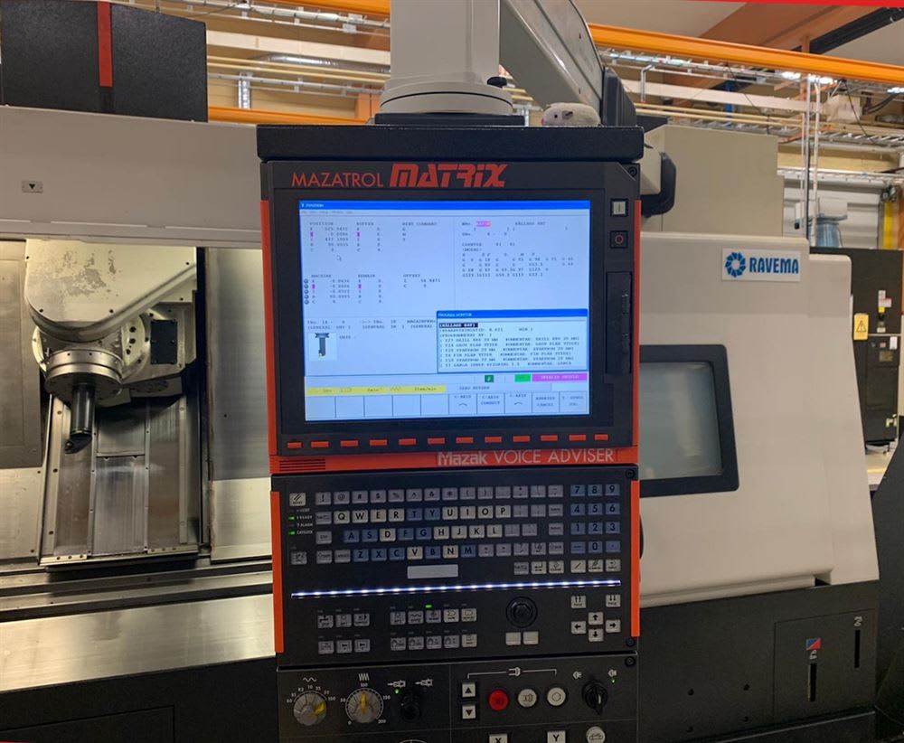 Mazak Mazatrol Matrix CNC machine control panel showing program data and a keyboard, positioned in front of a CNC milling machine and a Ravena industrial machine.