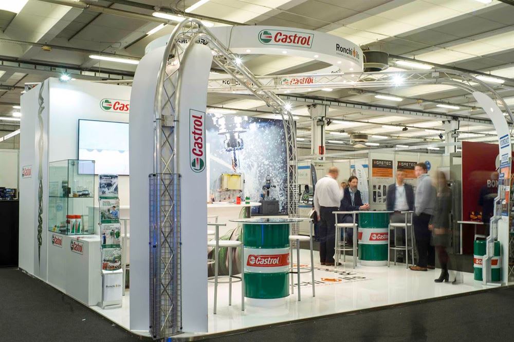 Stand espositivo Castrol e Ronchi con grande struttura ad arco in traliccio, schermi video, tavoli a forma di barile verde Castrol e persone che interagiscono.