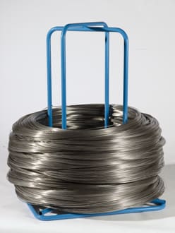 Gran bobina de alambre metálico gris enrollado sobre un soporte dispensador azul.