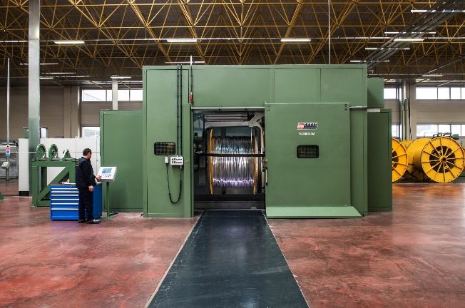 Worker operating a SAMAF TCB 1000-24M industrial wire and cable take-up machine with a large metal spool inside a manufacturing facility.