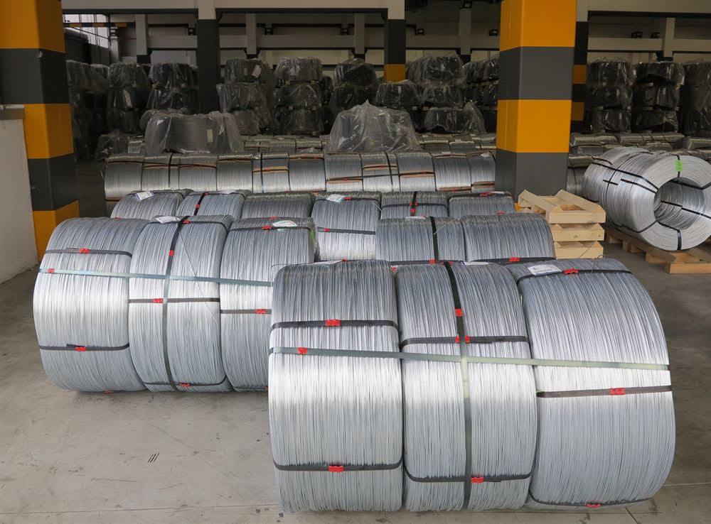 Rows of large coils of galvanized steel wire stacked on a concrete floor in an industrial warehouse.