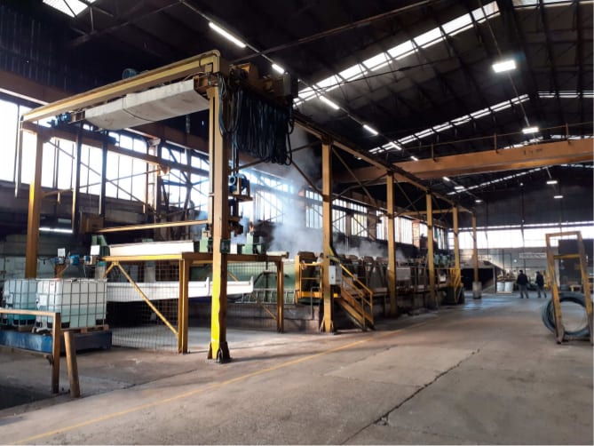 Impianto industriale con vasche di trattamento a vapore, carroponte e serbatoi chimici visibile all'interno di un capannone.