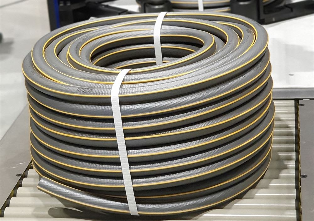 Rolled grey hose with a yellow stripe and textured surface, secured by white straps, on a roller conveyor.