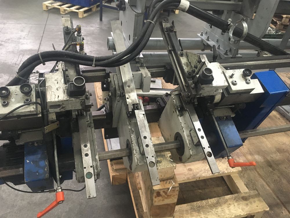 Macchinario industriale modulare con due teste di lavorazione motorizzate, cavi e manopole di regolazione, poggiato su pallet in un ambiente di fabbrica.