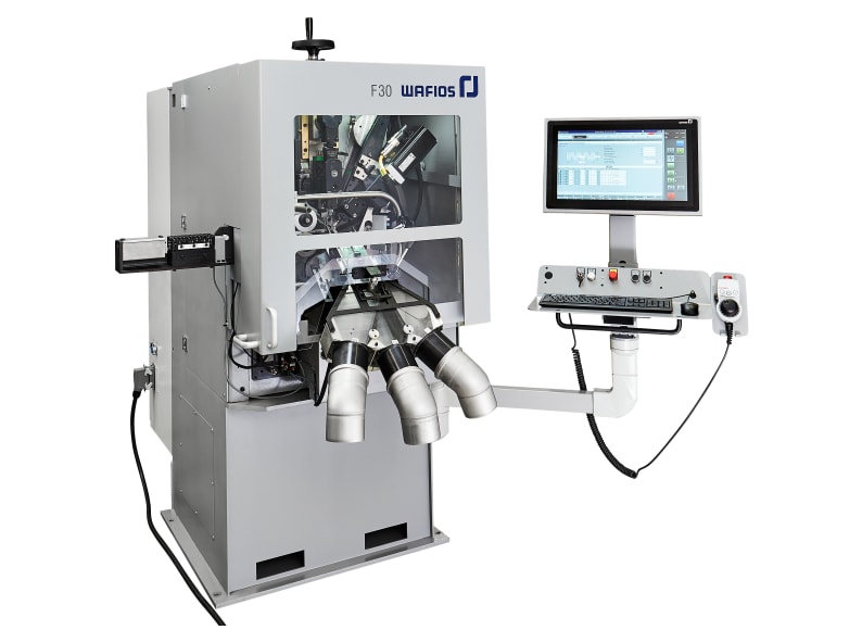 Macchina industriale WAFIOS F30 grigia per piegatura e formatura fili, con finestra trasparente che mostra i meccanismi interni, e un pannello di controllo digitale con monitor, tastiera e selettori, affiancata da tre uscite per i pezzi lavorati.