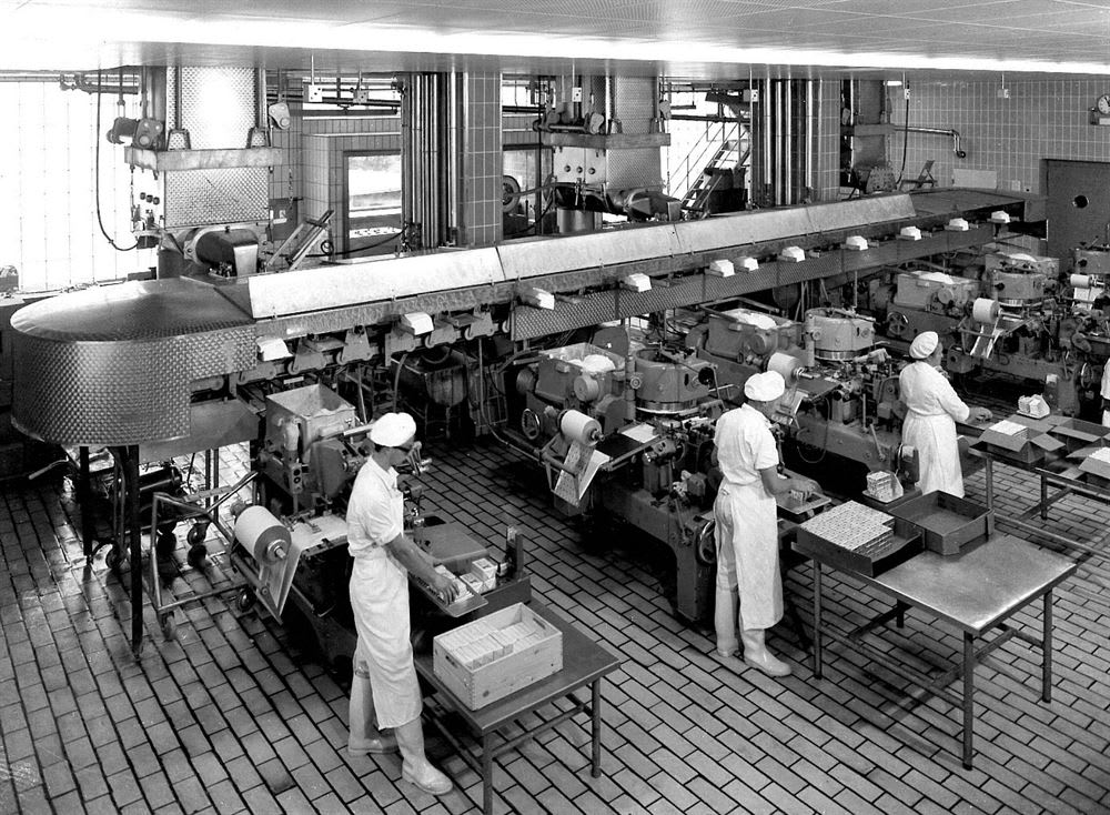 Workers in white uniforms packaging products on an industrial production line in a food processing factory.