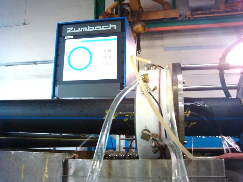 Industrial Zumbach measurement system monitoring a black plastic pipe with water cooling during an extrusion process.