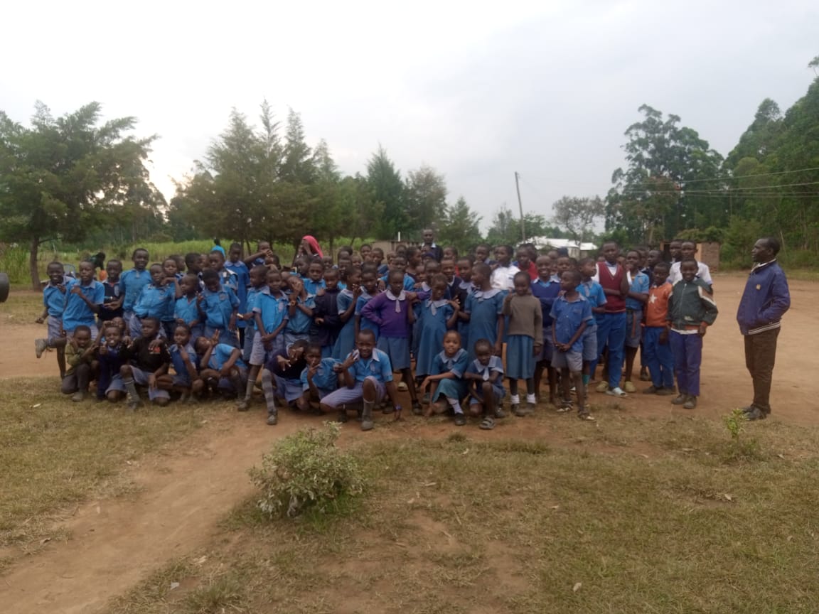 Group of smiling Kenyan school children in green uniforms standing outside a classroom