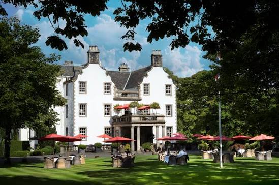 White 17th-century facade of Prestonfield House with parkland and Arthur's Seat behind
