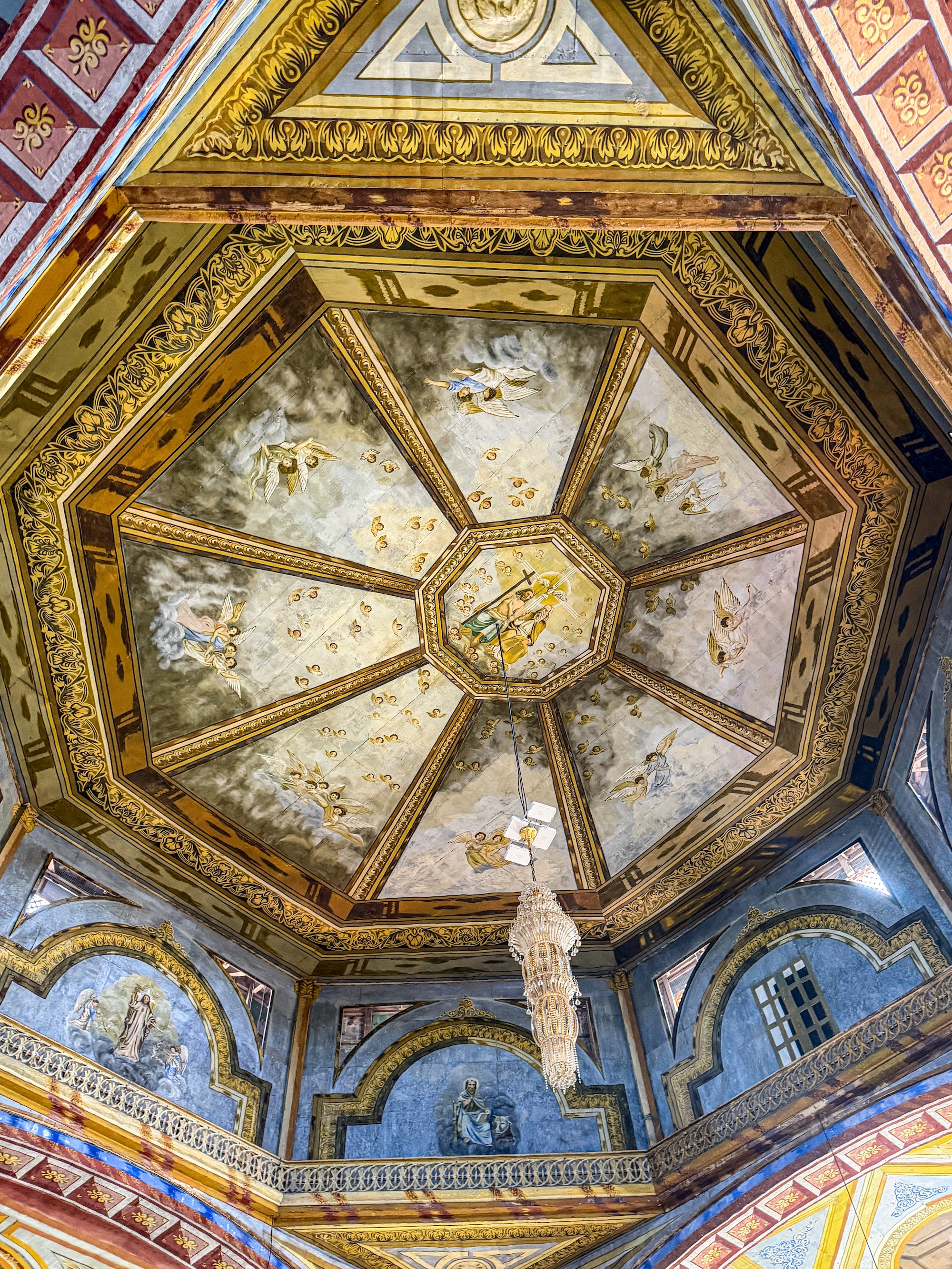 Ornate painted dome ceiling of Panglao Church with angel murals and a hanging chandelier
