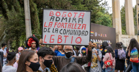 a group of masked people at a protest in Bogota, one man holds up a sign that reads 'Bogota admira la fortaleza de la comunidad LGBTIQ