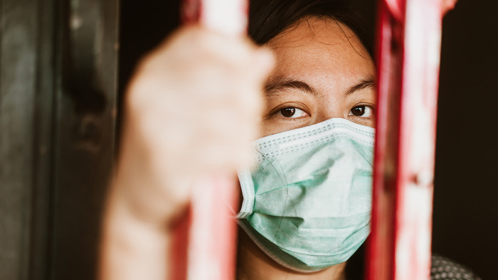 Asian woman wearing mask behind bars