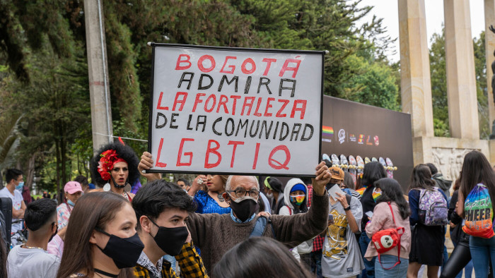 a group of masked people at a protest in Bogota, one man holds up a sign that reads 'Bogota admira la fortaleza de la comunidad LGBTIQ