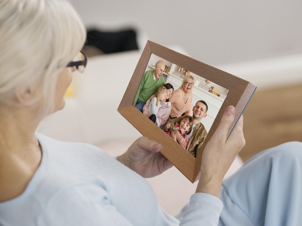 O bunică se uită, în rama ei Familink, la o fotografie a familiei sale