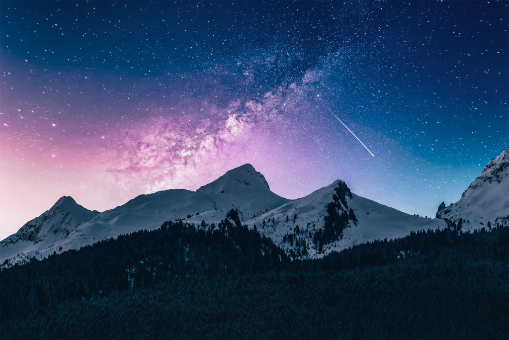 Mountains with snow with a night sky showing stars and a galaxy