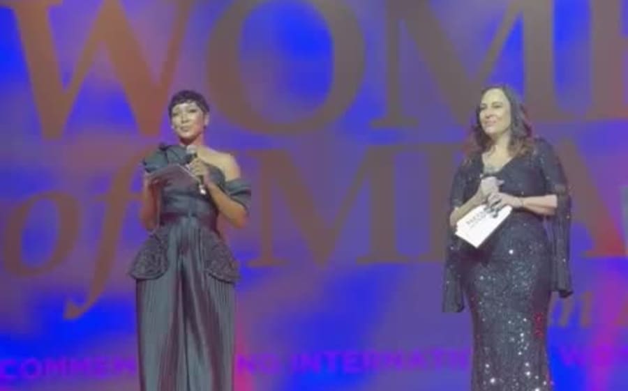 Yolanda Robert presenting on stage with a microphone under stage lighting