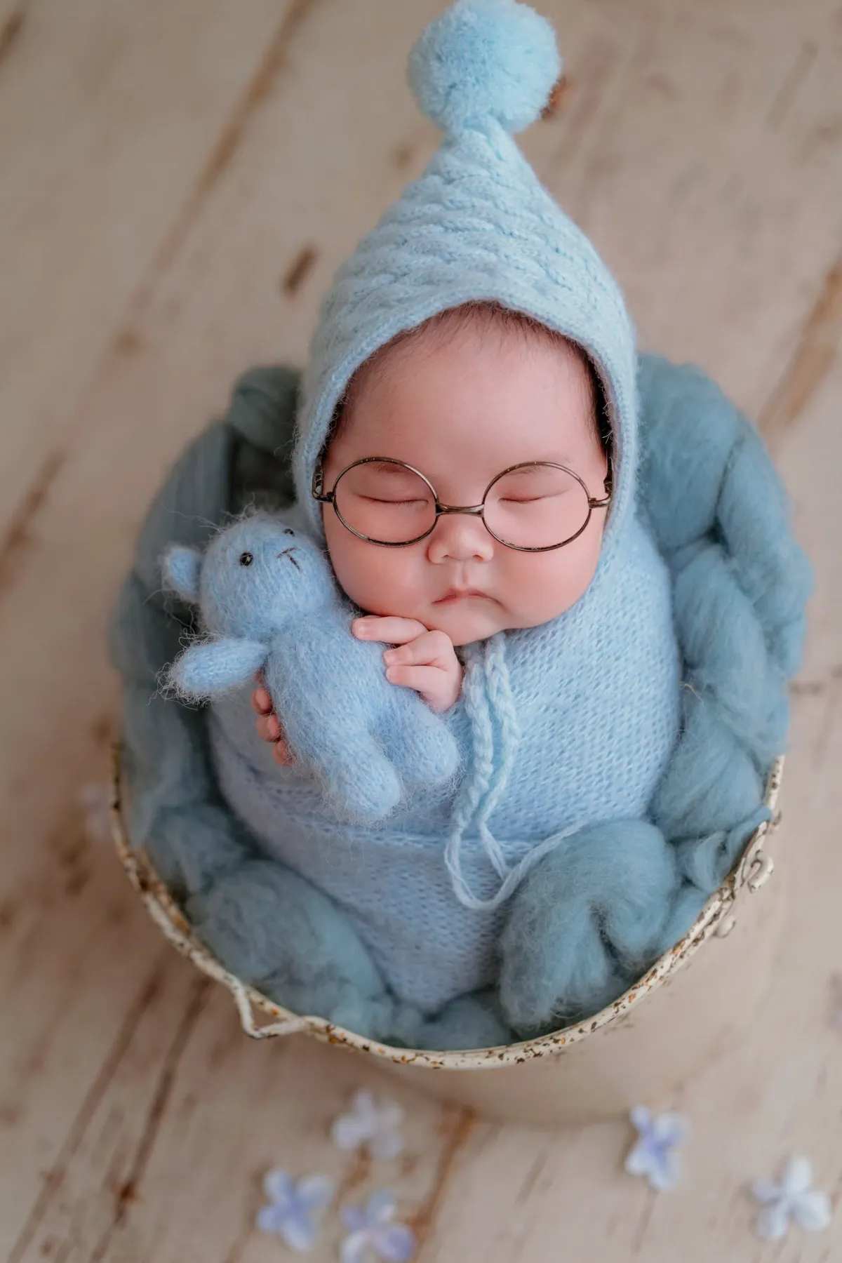Bé sơ sinh nằm ngủ trong giỏ, đội mũ len xanh — những ngày đầu đời bắt đầu lịch tiêm chủng cho bé