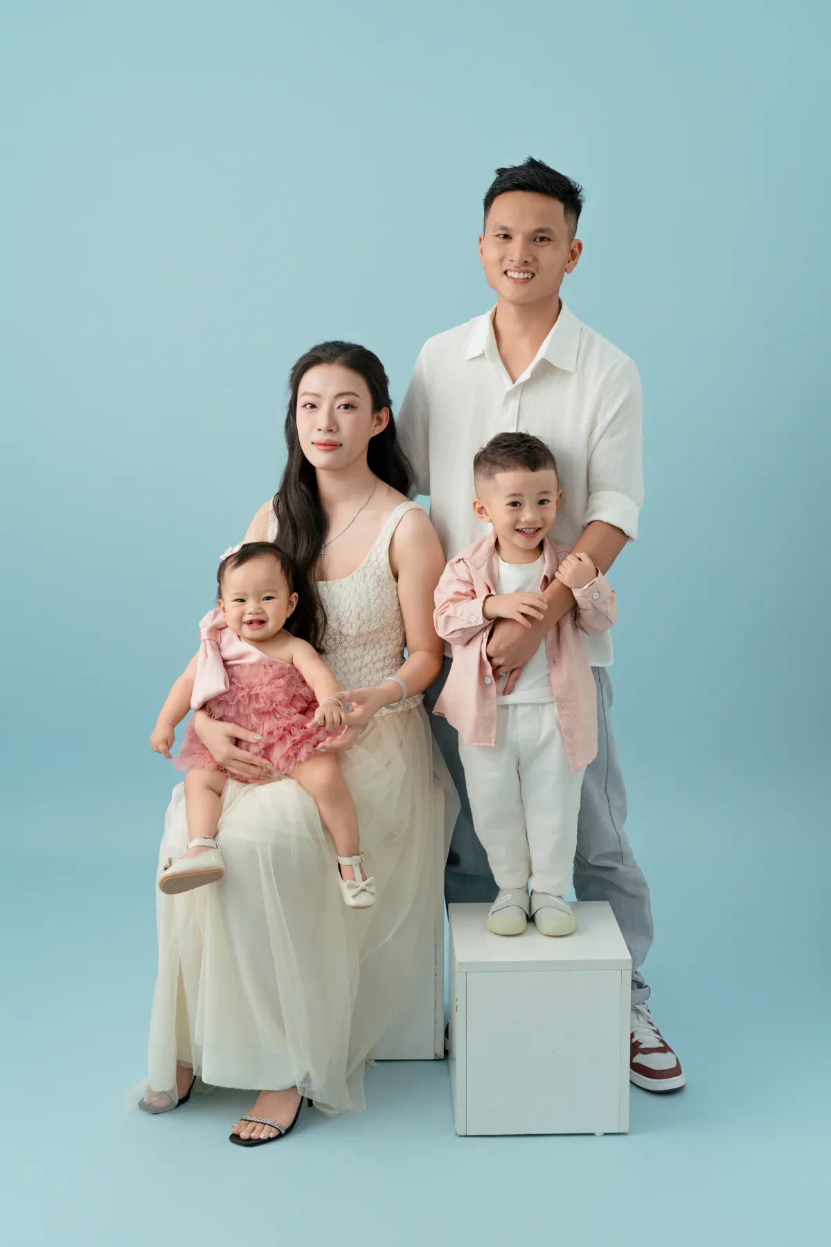 Gia đình bốn người trên nền xanh — bé trai và bé gái cùng ba mẹ đi chơi cuối tuần Đà Lạt cùng bé