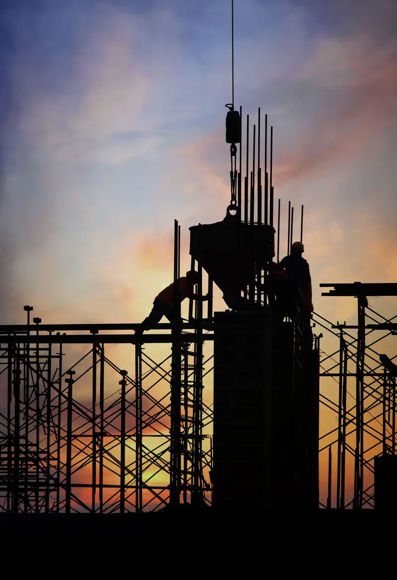 Construction workers and crane silhouetted at sunset