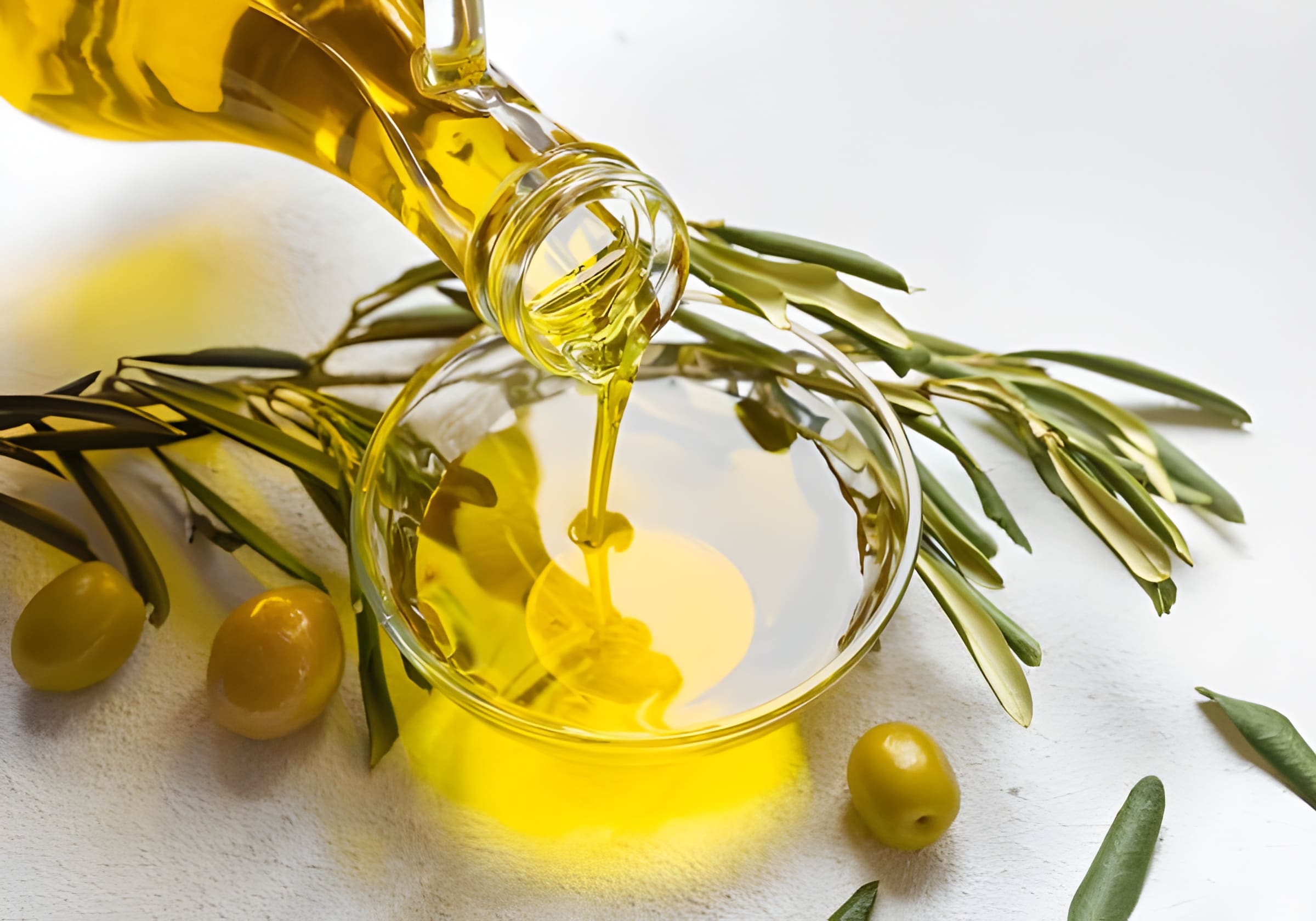 Golden oil poured into a glass bowl beside an olive branch