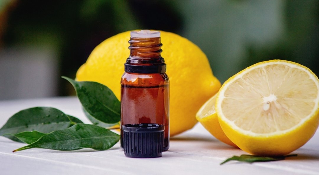 Lemon oil bottle beside fresh lemons and leaves