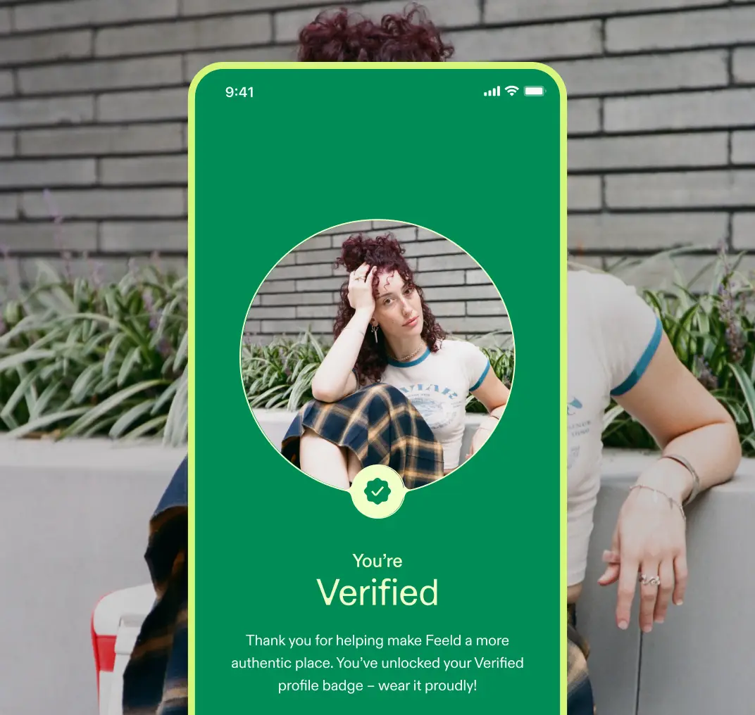 A green screen reading "You're Verified" with a circular photo of a person with curly auburn hair. A green verified checkmark sits below the photo, with text: "Thank you for helping make Feeld a more authentic place. You've unlocked your Verified profile badge - wear it proudly!"