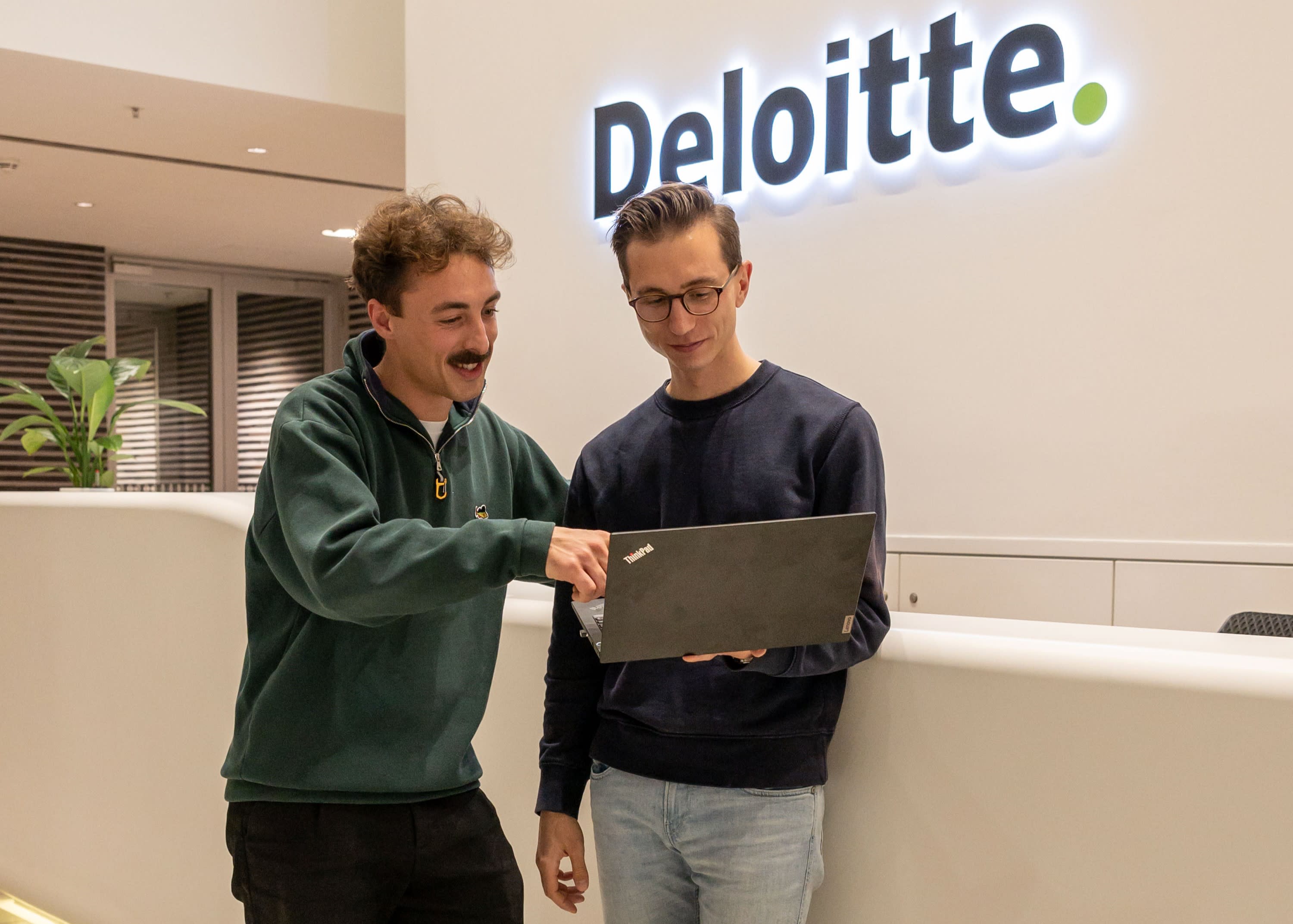 Zwei Personen stehen in einem Büro von Deloitte und besprechen Inhalte auf einem Laptop.