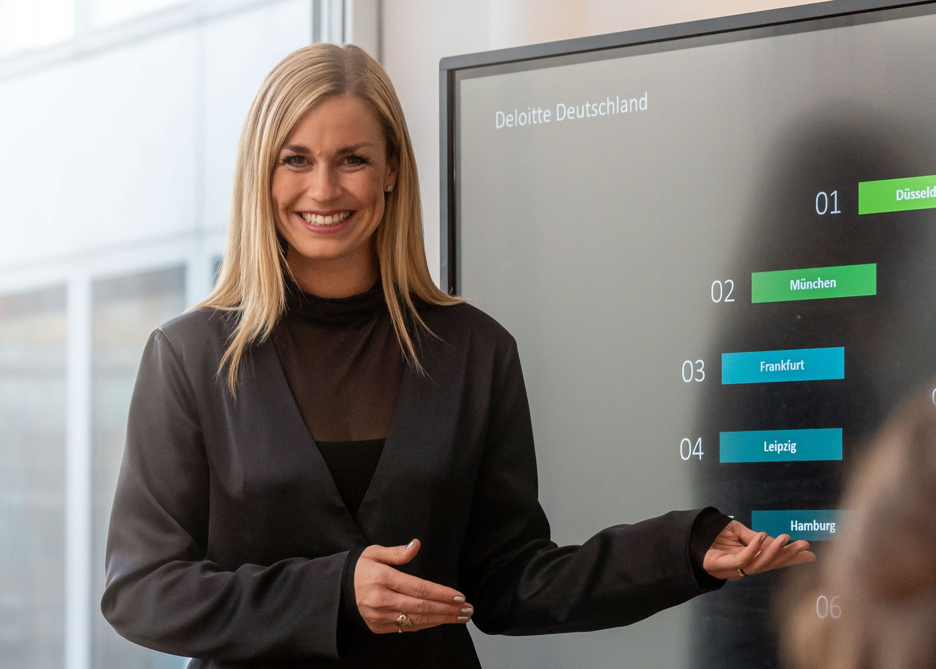 Person präsentiert vor einem Bildschirm mit Standorten von Deloitte in einem Besprechungsraum.
