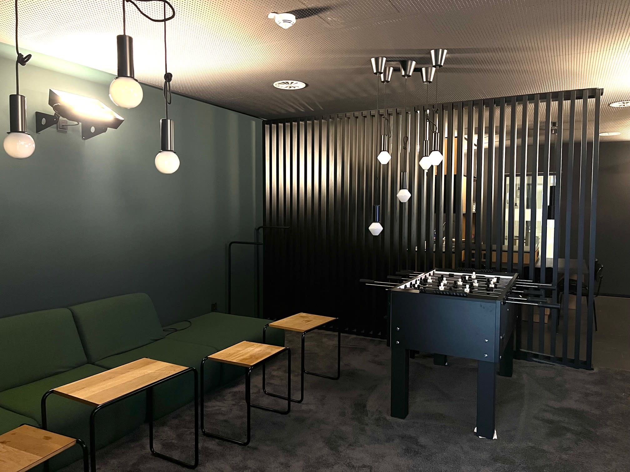 Moderner Loungebereich mit grünem Sofa, Beistelltischen, Kicker und Lamellenwand.