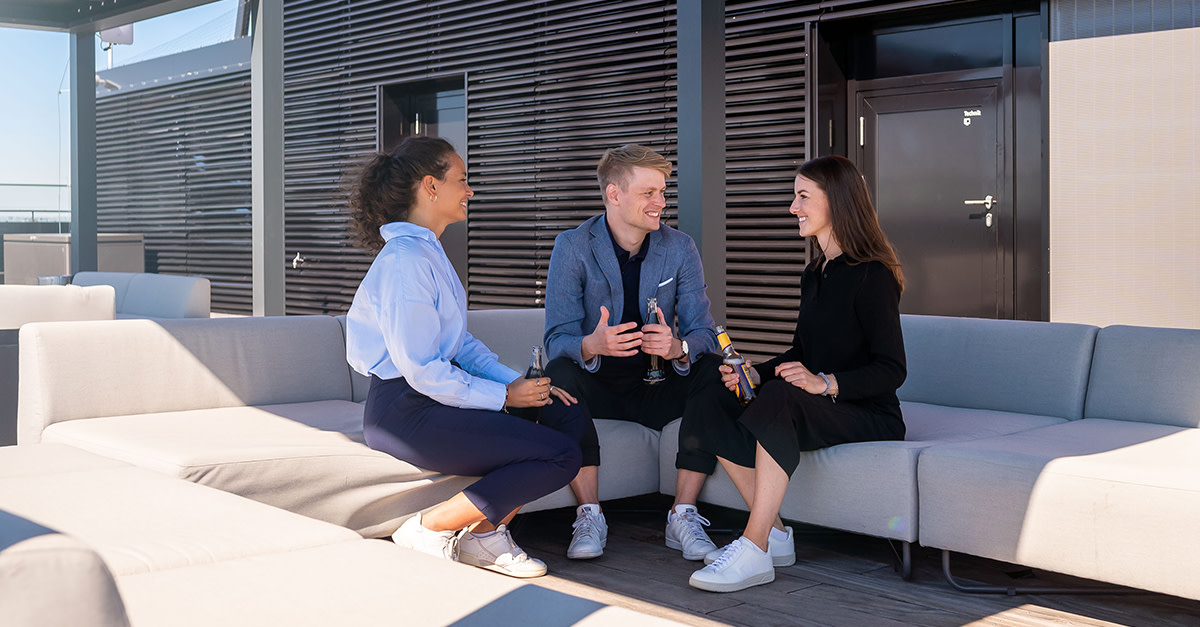 Drei Personen sitzen auf einer modernen Dachterrasse auf Sofas und unterhalten sich bei gutem Wetter