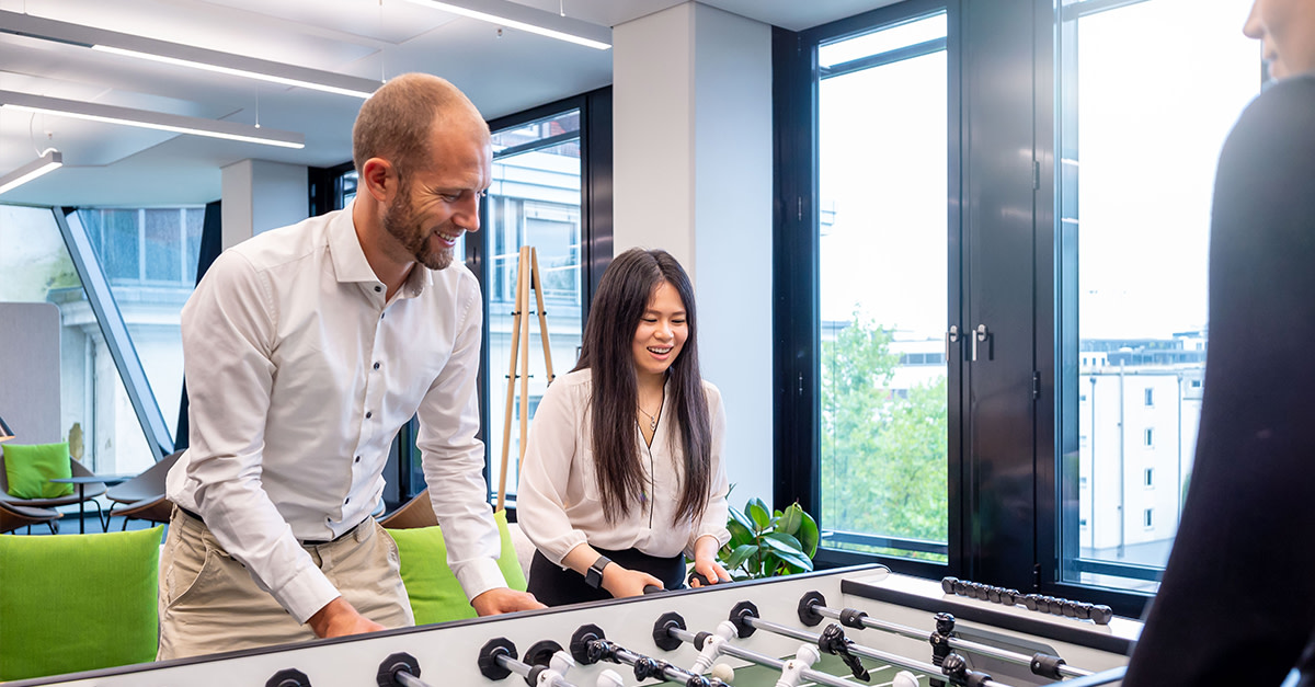 Kolleg:innen spielen gemeinsam Fußball-Kicker im hellen Büro in ihrer Pause.