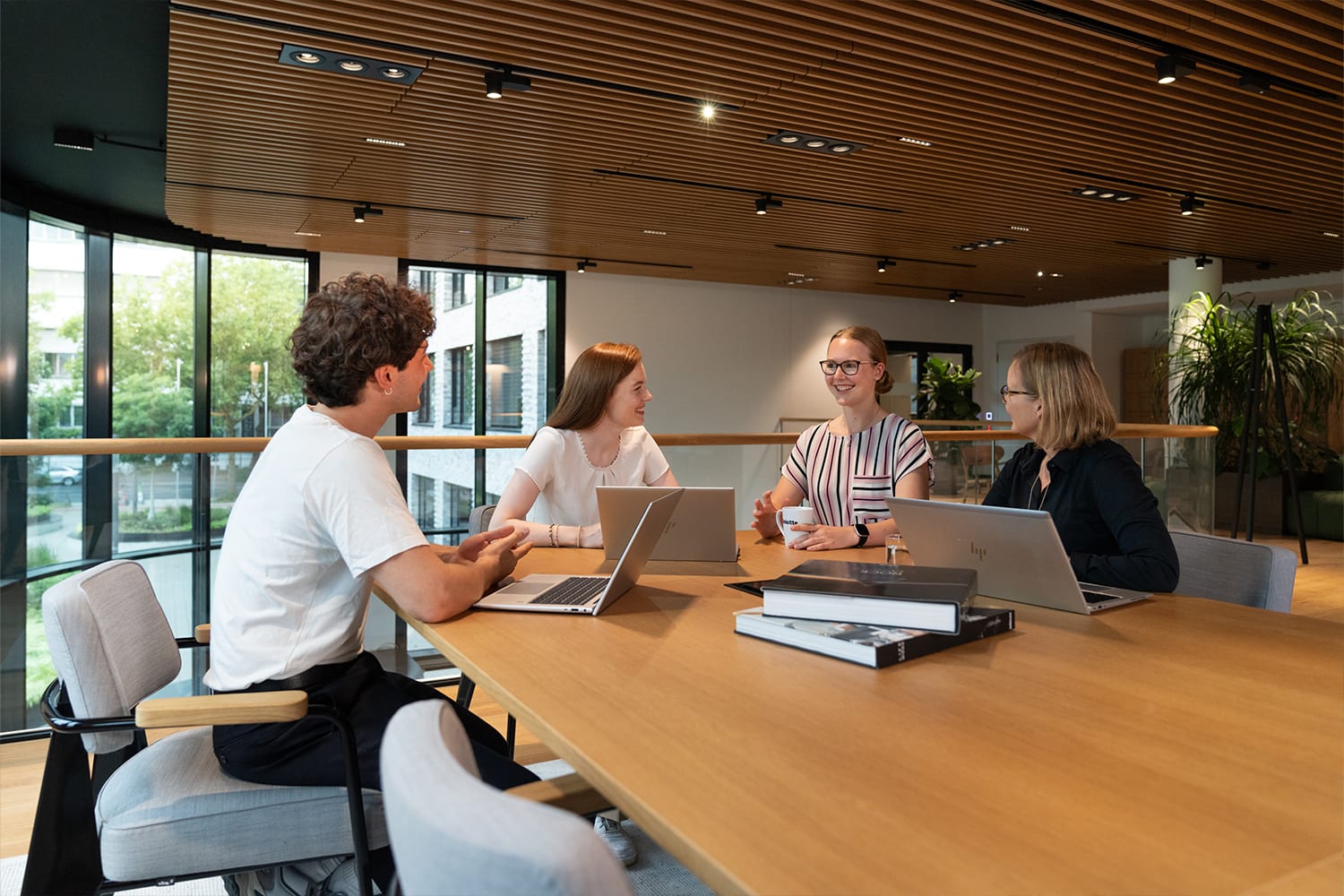 Mehrere Kolleg:innen, die an einem Tisch mit Laptops sitzen und sich unterhalten