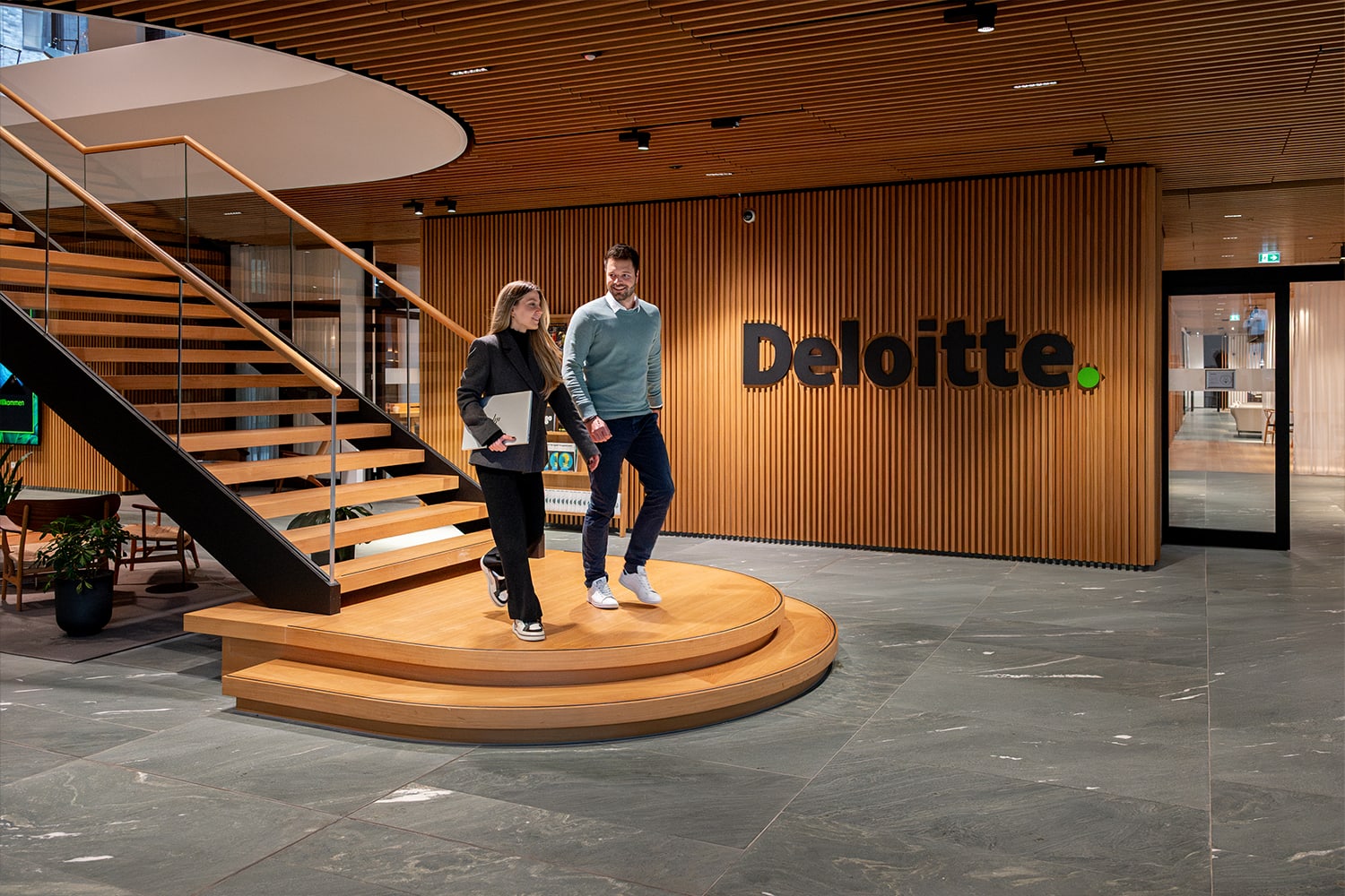 Zwei Kolleg:innen, die eine Treppe runterlaufen im Eingangsbereich von Deloitte