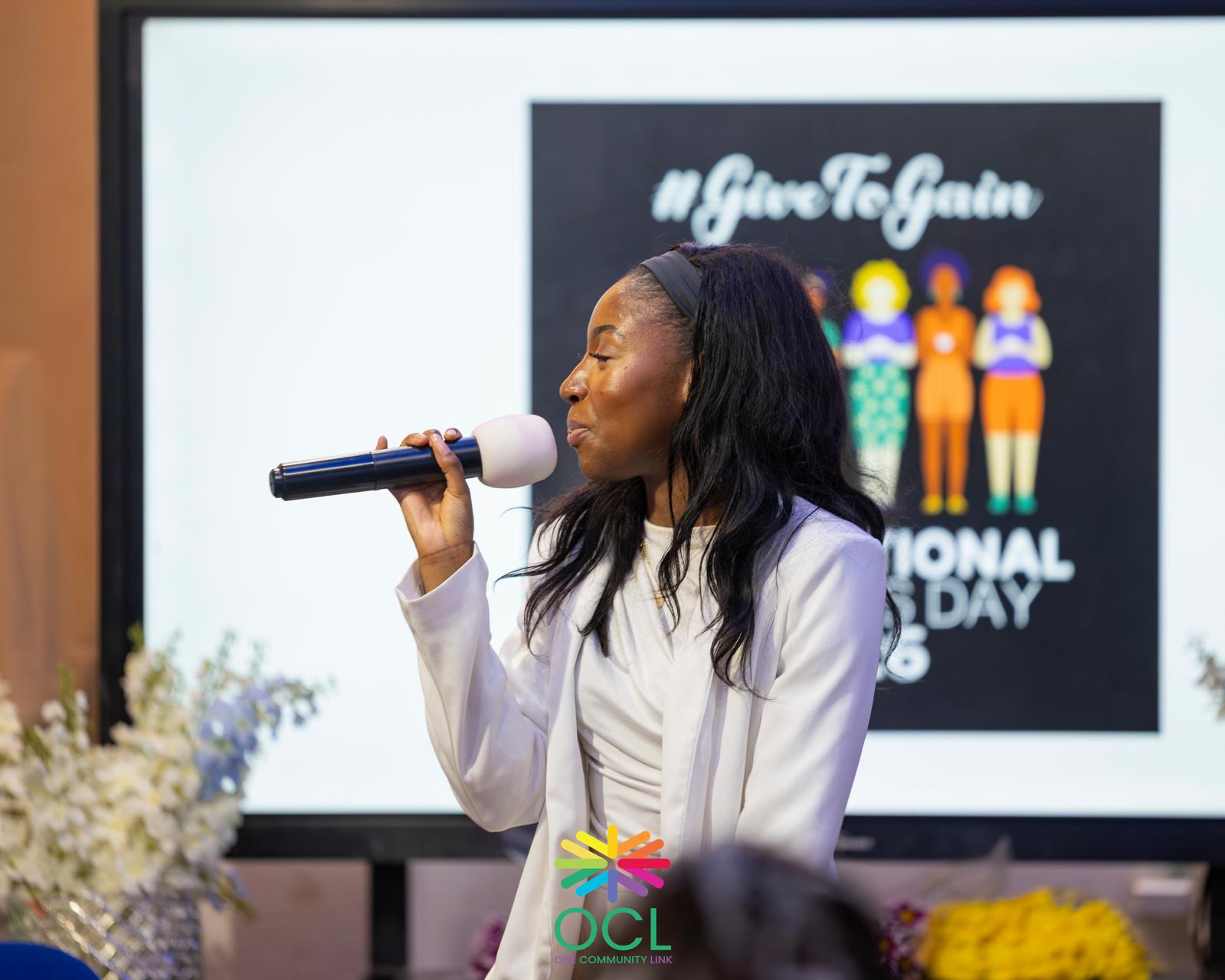 A speaker addresses a One Community Link event with an International Women's Day display behind her.