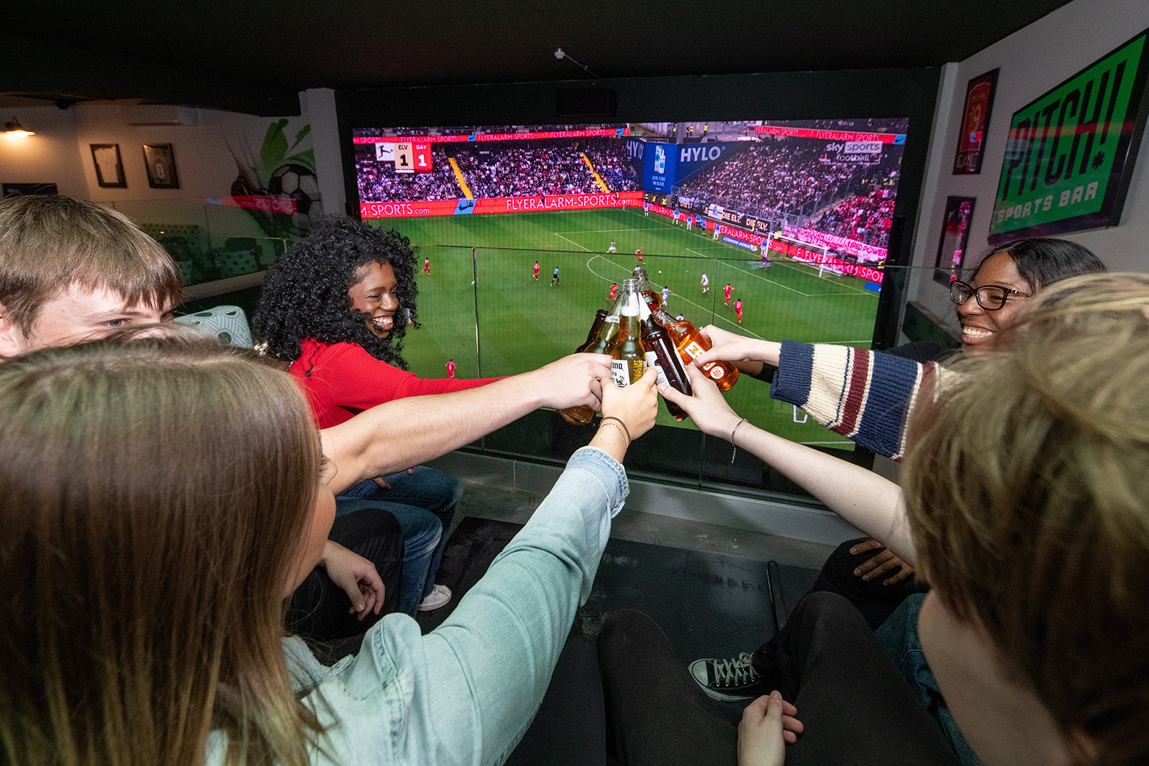 Friends raise drinks in front of a large football screen inside Pitch Sports Bar in Middlesbrough.