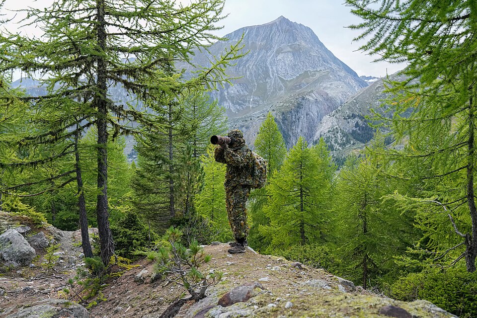 A wildlife photographer in camouflage outdoors in Switzerland; illustrative image, not the student featured.