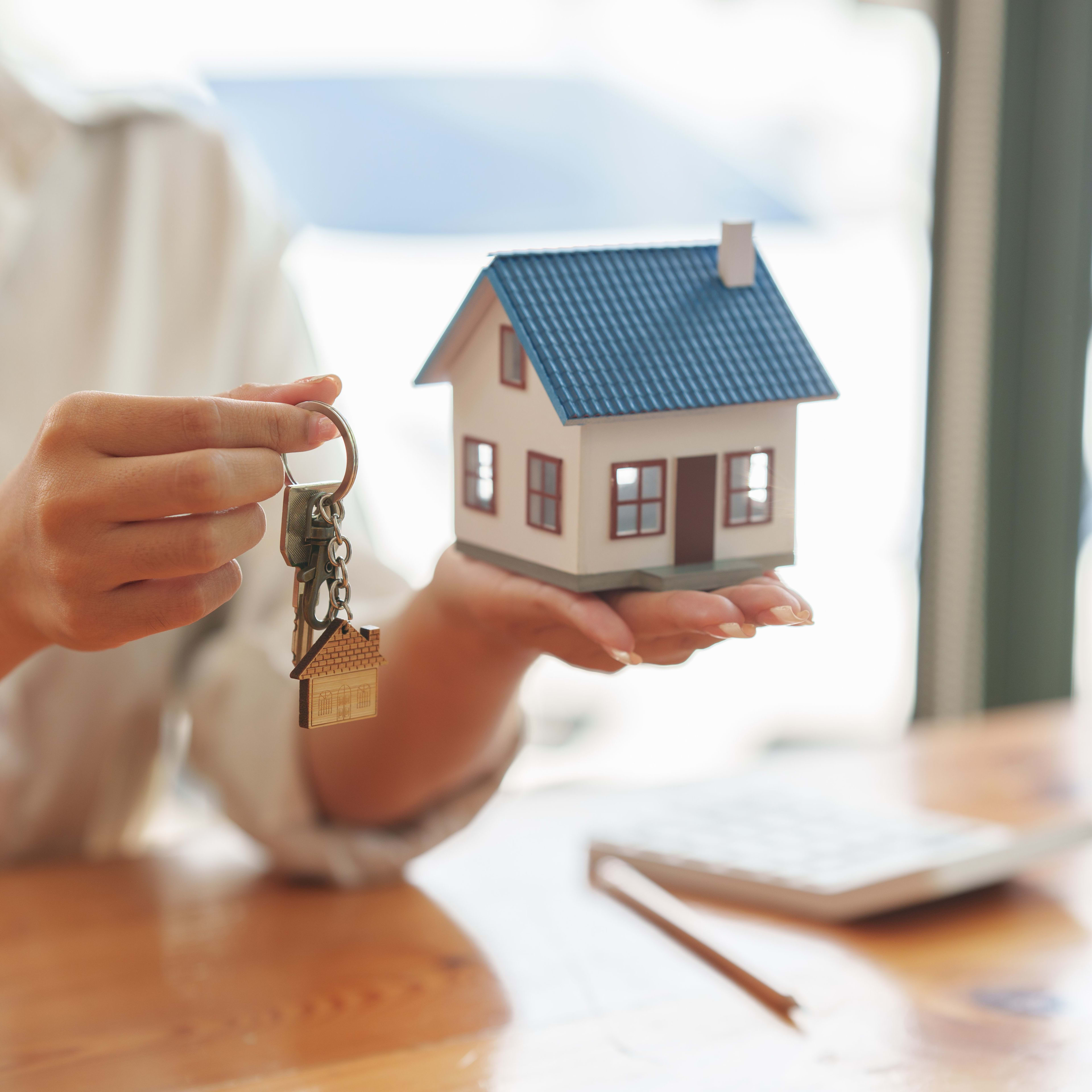 Kleines Modell eines Hauses, das auf schützend auf einer offen Handfläche platziert ist