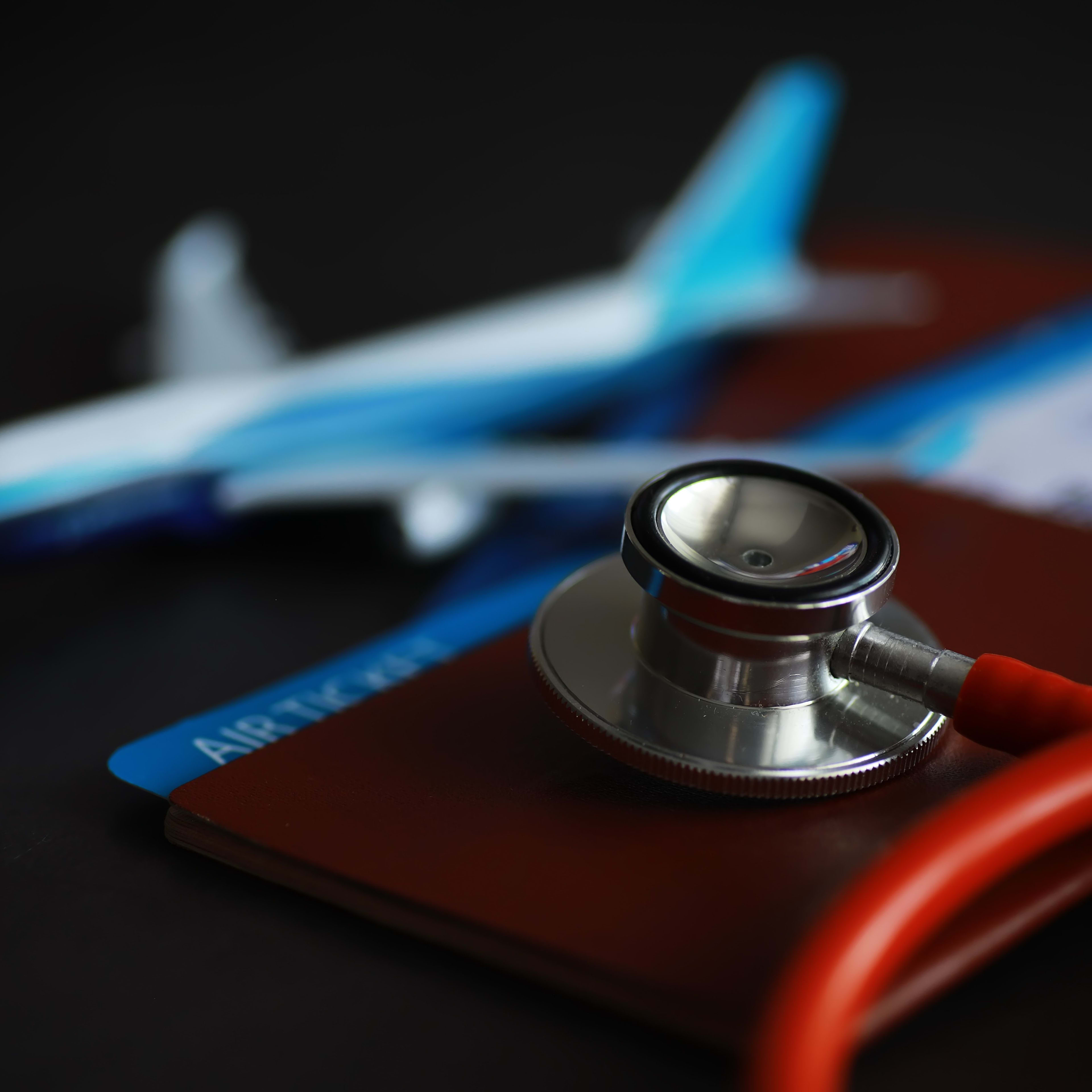 Kleines Flugzeugmodell, das zusammen mit einem Stethoskop und einem Reisepass auf dem Tisch liegt 