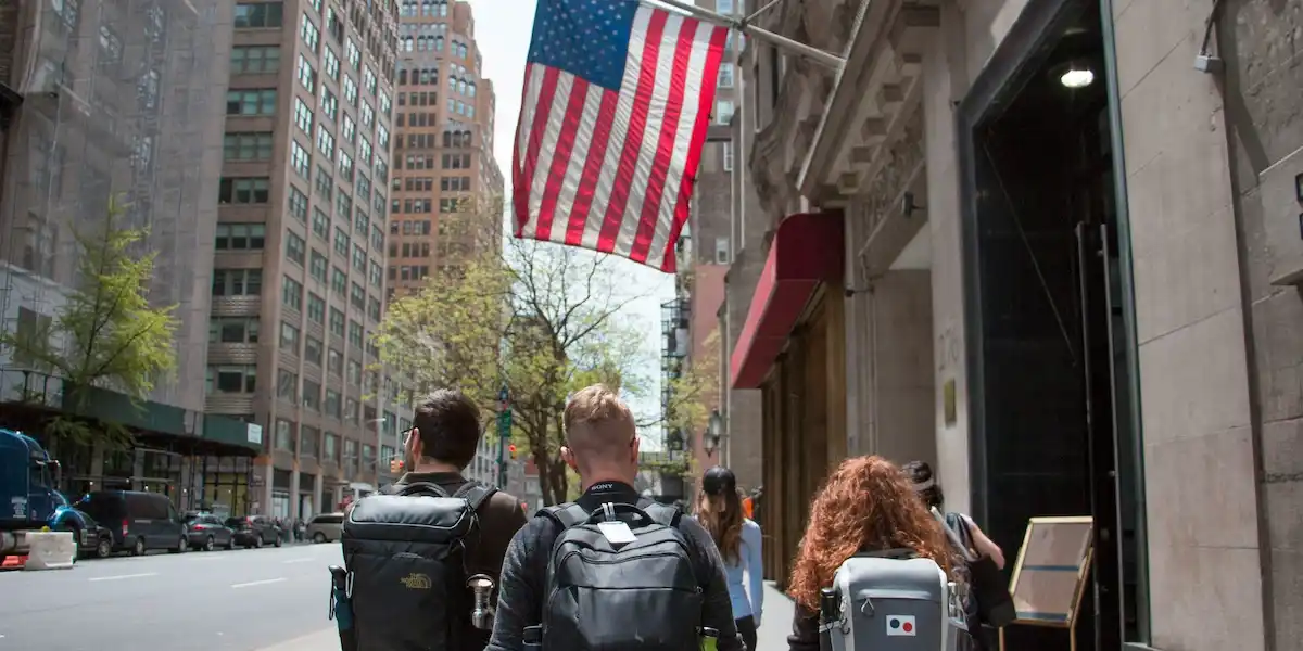 Illustrative: Students walking through a U.S. city with backpacks beneath an American flag—used as an illustrative image for a student loan policy guide.
