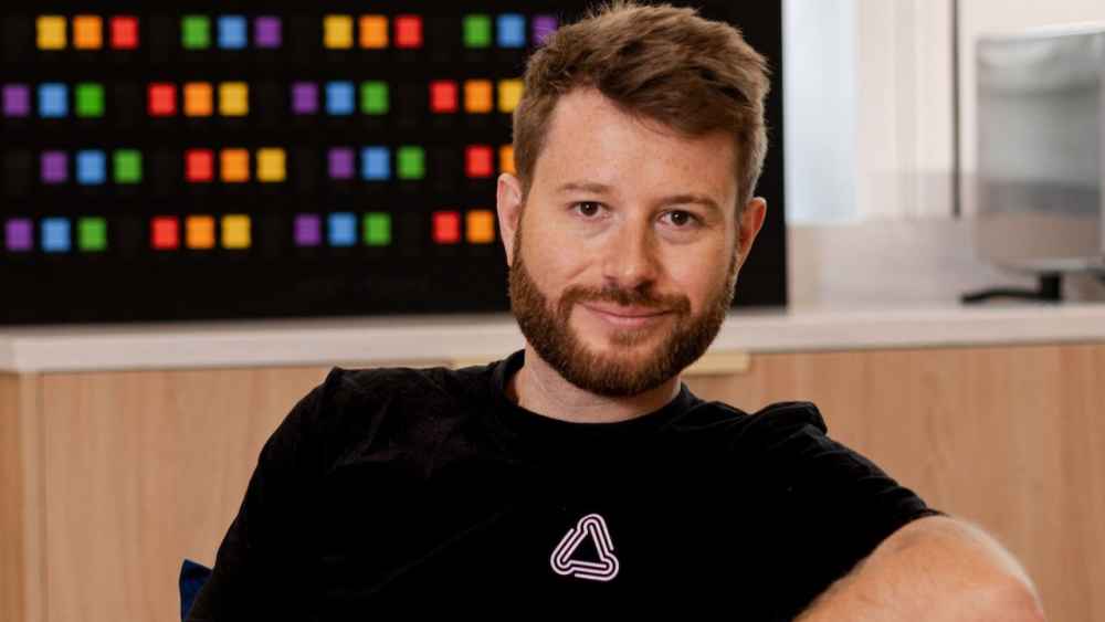 Theo Saville, CEO of CloudNC, seated indoors in front of a multicolored wall display.